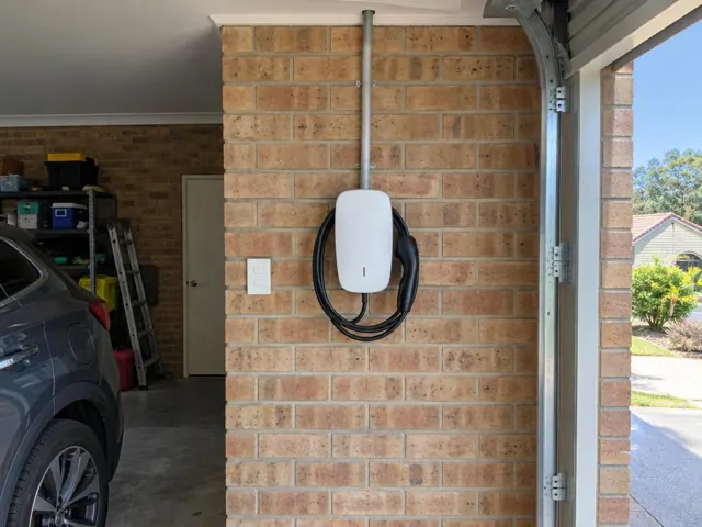 Wall-mounted EV charger on a brick garage wall beside a car and storage shelves in Nerang